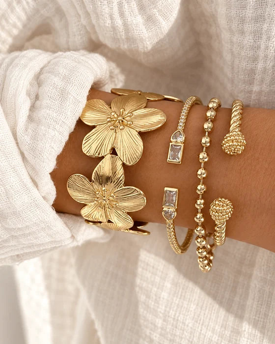 Gold bracelets with floral details worn on a wrist