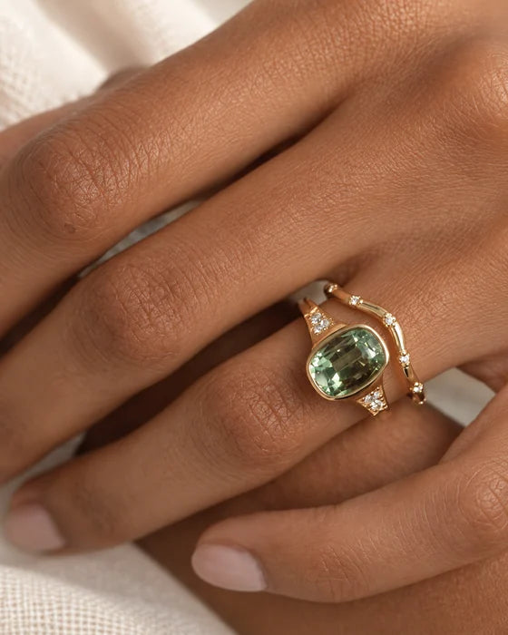 Gold rings with green and clear stones worn on a hand